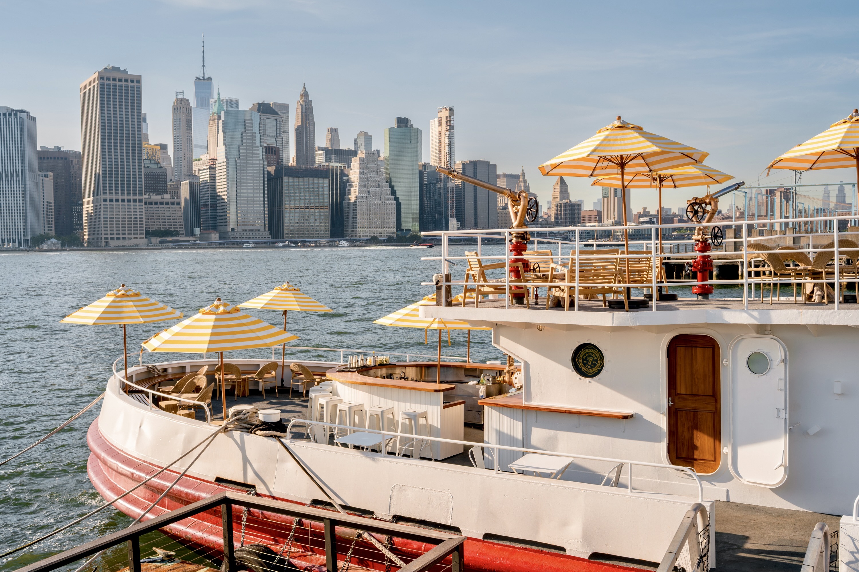 A white boat with yellow umbrellas with Manhattan's skyline in the background.