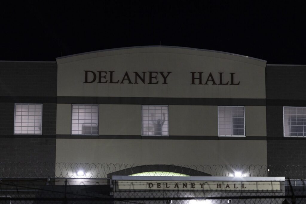 A detainee stands silhouetted in a window of the Delaney Hall detention center in Newark, N.J., on May 28, 2026. Many federal judges are freeing immigrants held under a mandatory detention policy. (Photo by Anne-Marie Caruso/New Jersey Monitor)