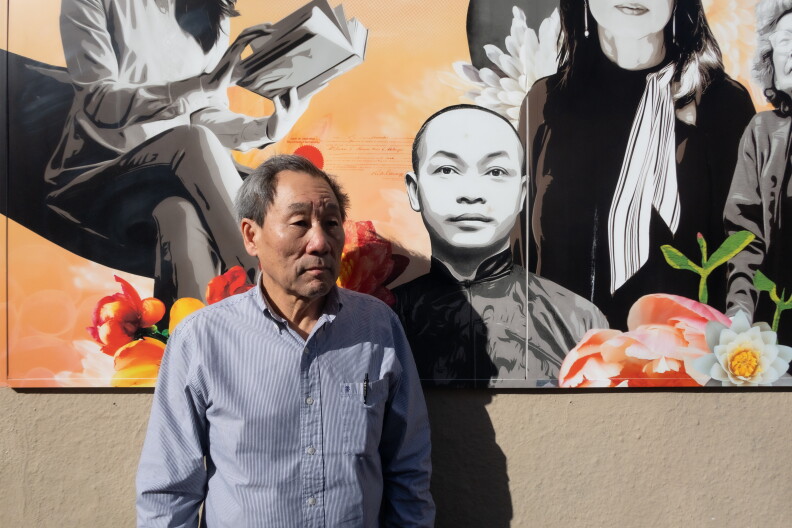 An Asian American man in his 70s stands in front of a mural of Asian American and Pacific Islander leaders.