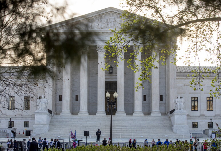 People stand around and on a stage in front of the Supreme Court.