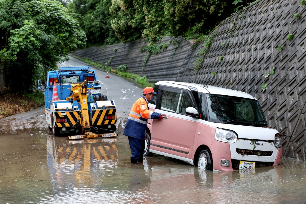 A tow lorry driver retrieves a partially submerged car after flooding in the town of Kashiwara, Osaka prefecture on June 26, 2026. Photo: Paul Miller/AFP.
