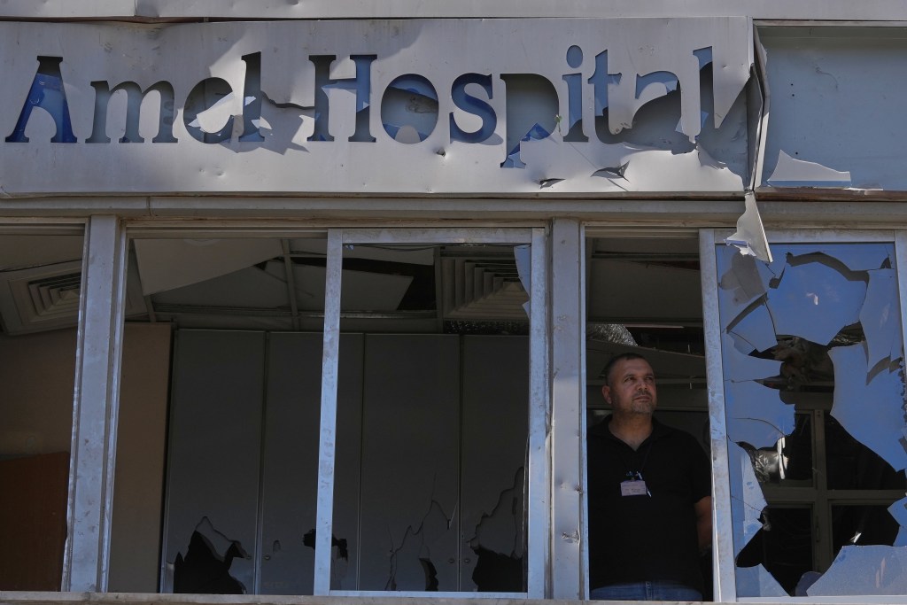 A person stands in a building with broken windows looking out.