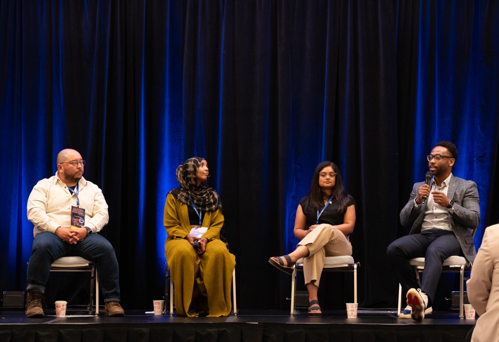 four speakers on a stage at a conference, with blue background