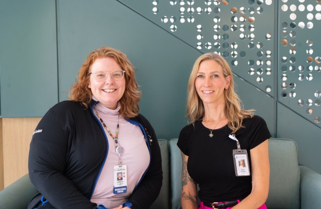 Two women wearing lanyards sit smiling in chairs.