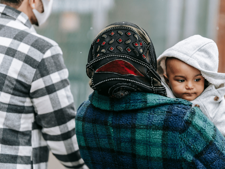 Asylum seeker story: A couple walking outside and the woman is holding a toddler. Only his face is visible.