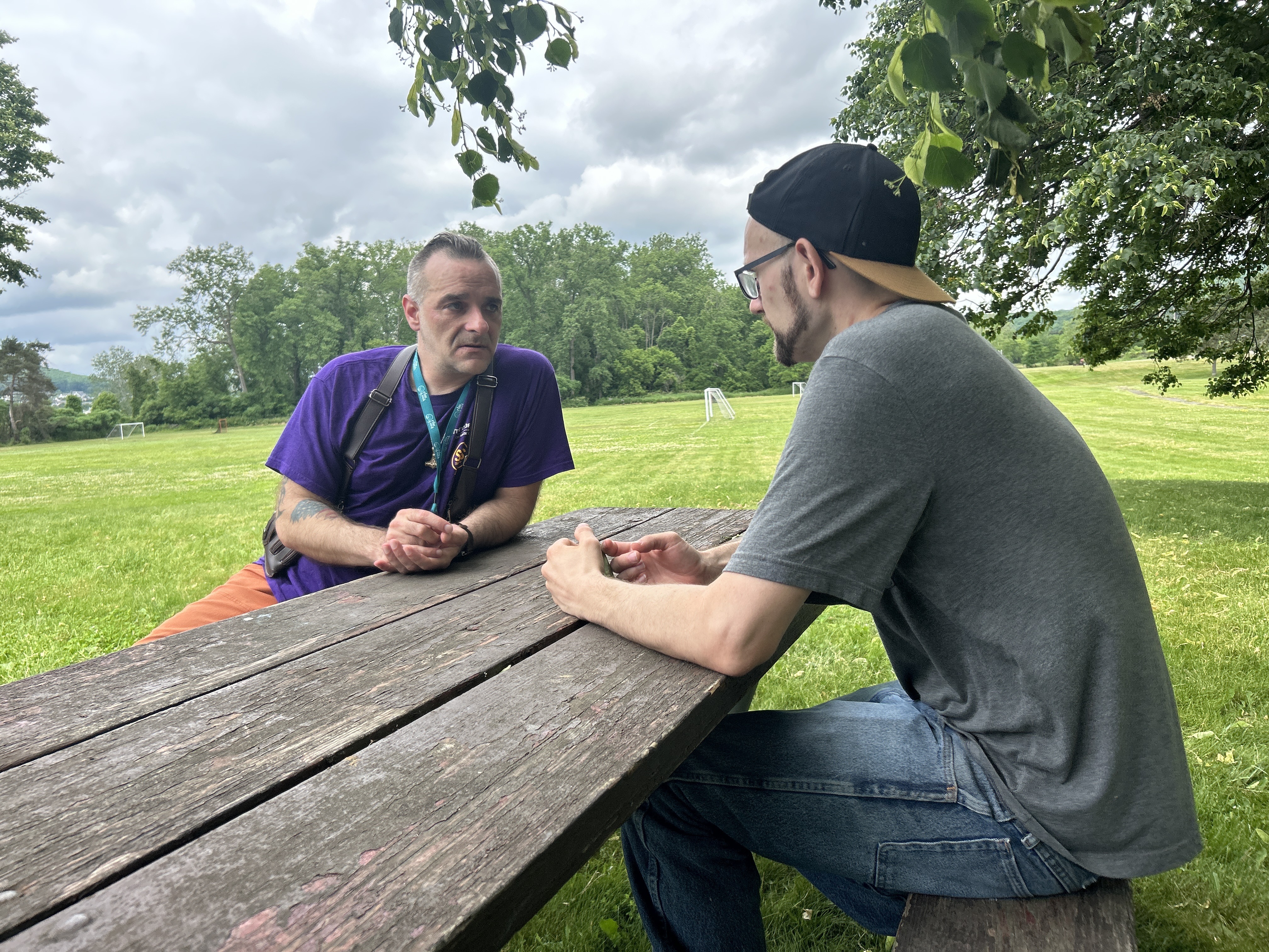 Two men sitting on a picnic table have a chat.