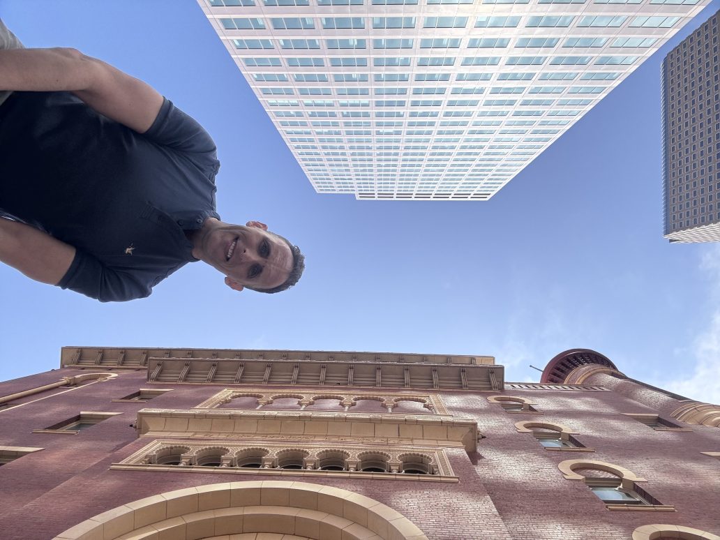 A man takes a selfie with Denver buildings
