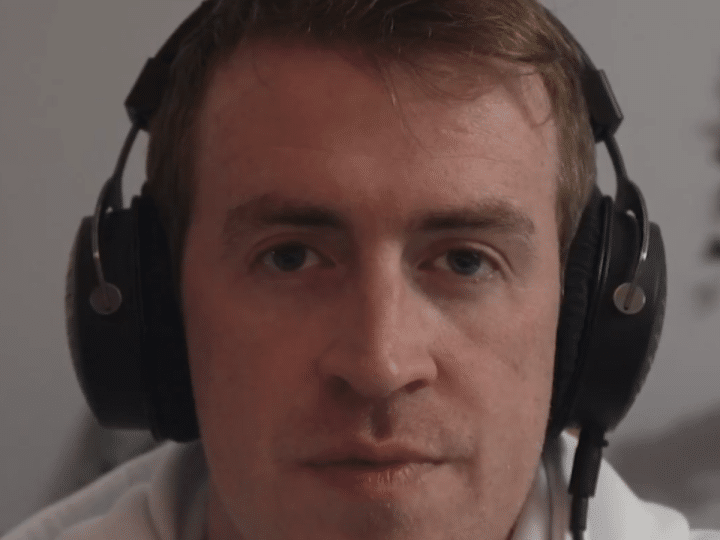 A screenshot of Irish Michael McCarthy speaking on this video, wearing headphones