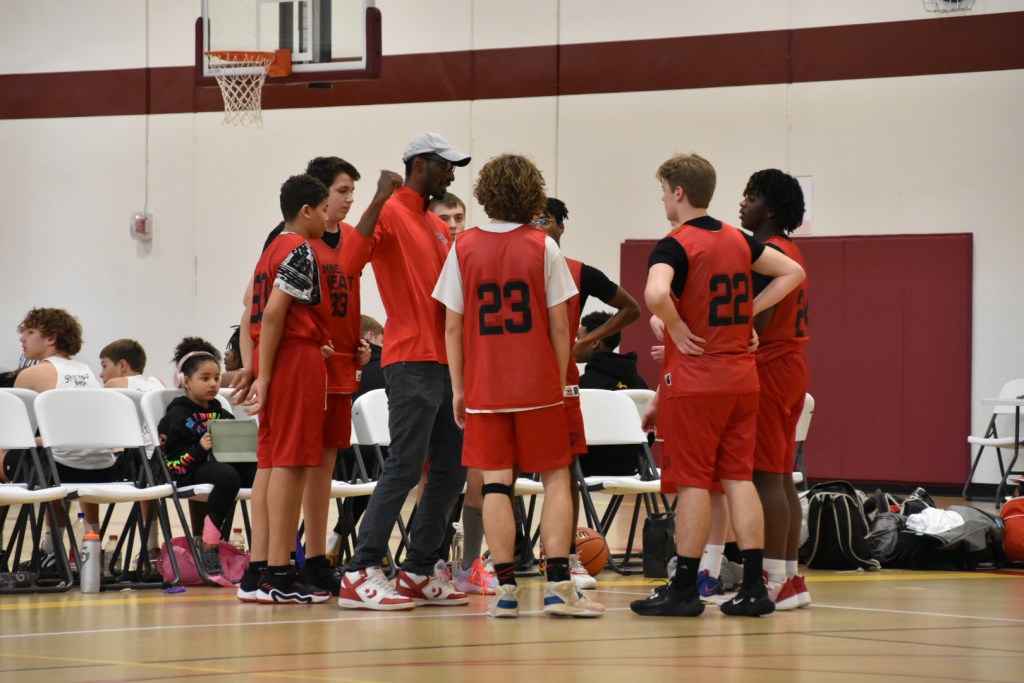 Coaches talk to a group of young men in red basketball uniforms on a basketball court.