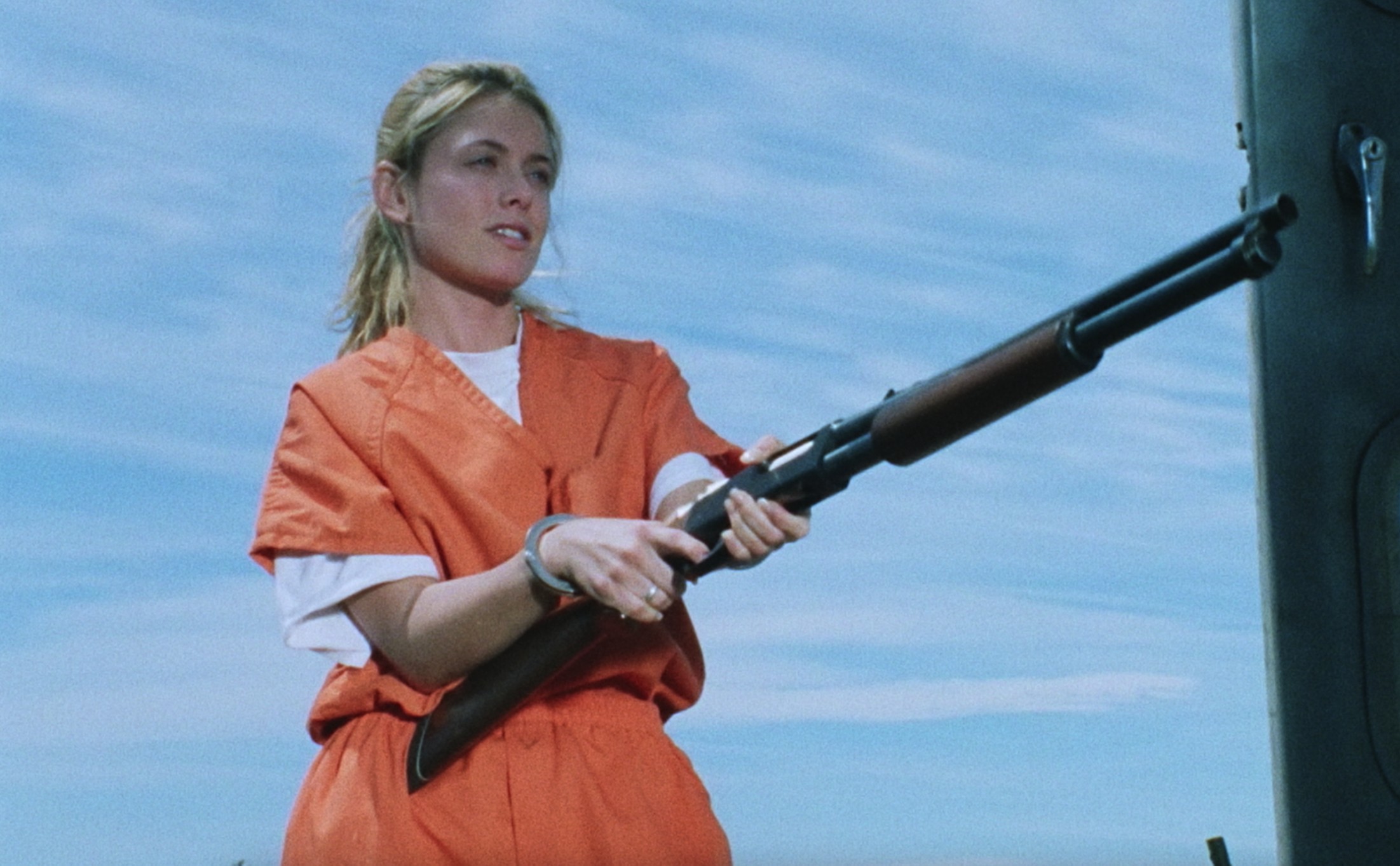 A woman in orange prison scrubs with a gun