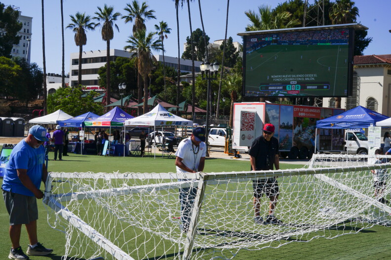 Three men replace the netting on soccer goal posts.