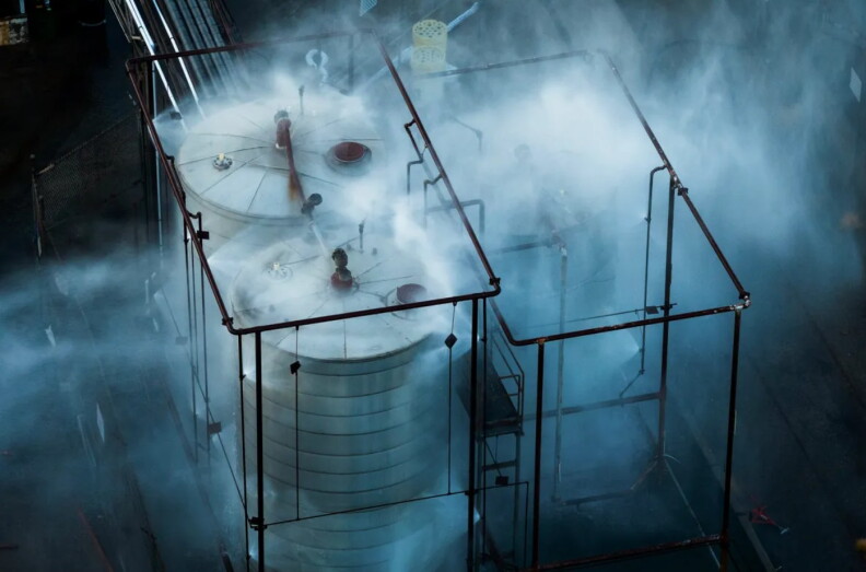mist and spray surrounds a pair of large metal tanks flanked by piping and scaffolding.