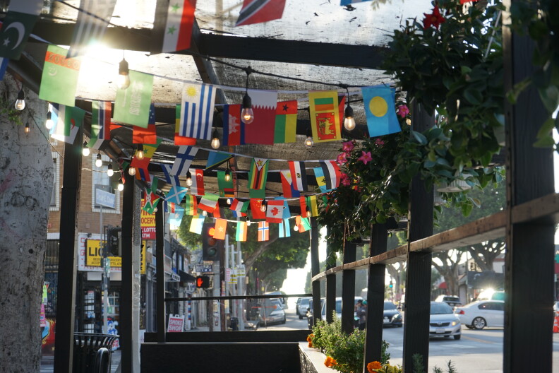 Multi-colored flags are strewn across the roof of an empty outdoor patio area. Cars are seen passing in the distance. 