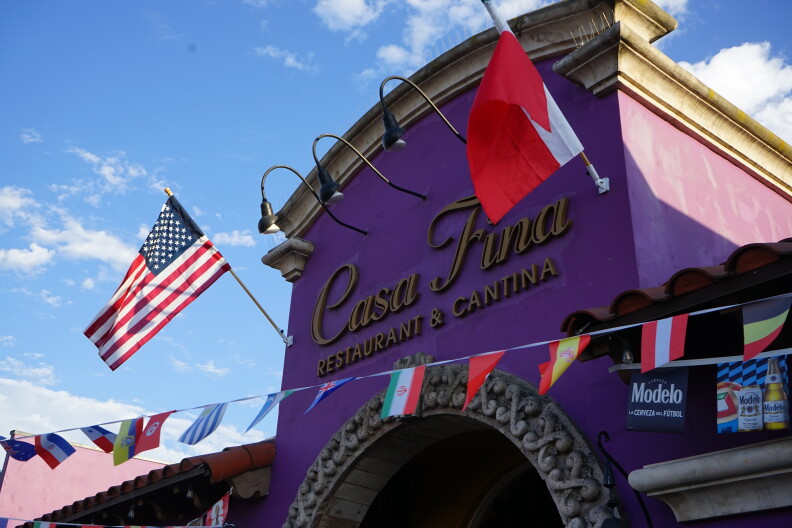 A string of international flags are strewn across the exterior of a purple building. Letters on the building read "Casa Fina Restaurant & Cantina".
