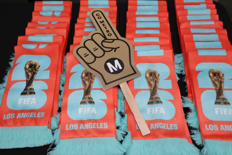 Multi-colored scarves are displayed with the worlds "FIFA LOS ANGELES" printed on them. A sign with a pointed finger reads "METRO". 
