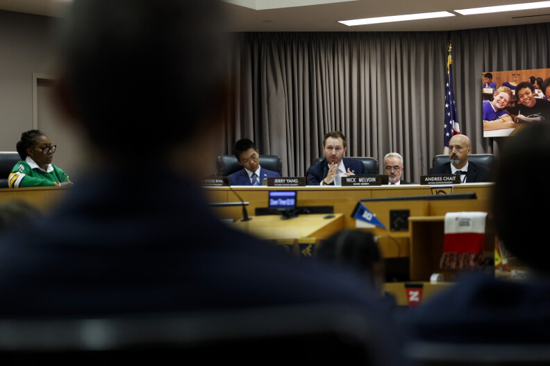 A distant view of a half circle of people in suits talking to a crowd.