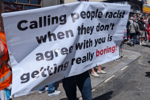 A sign a far-right protester is holding up which is black and red font on a white background which reads: Calling people racist when they don't agree with you is getting really boring.