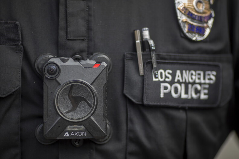Close up of a square body camera attached to an officer. The officer's shirt has a patch that reads "Los Angeles Police" and a police badge