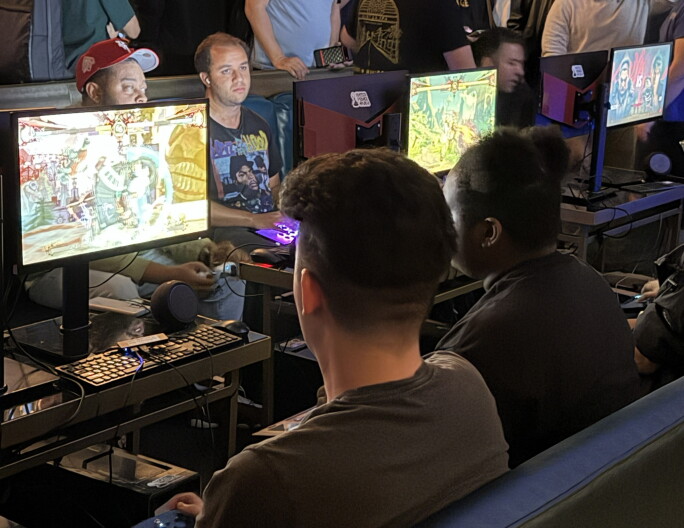 A group of people sitting in front of monitors and playing Street Fighter 6.