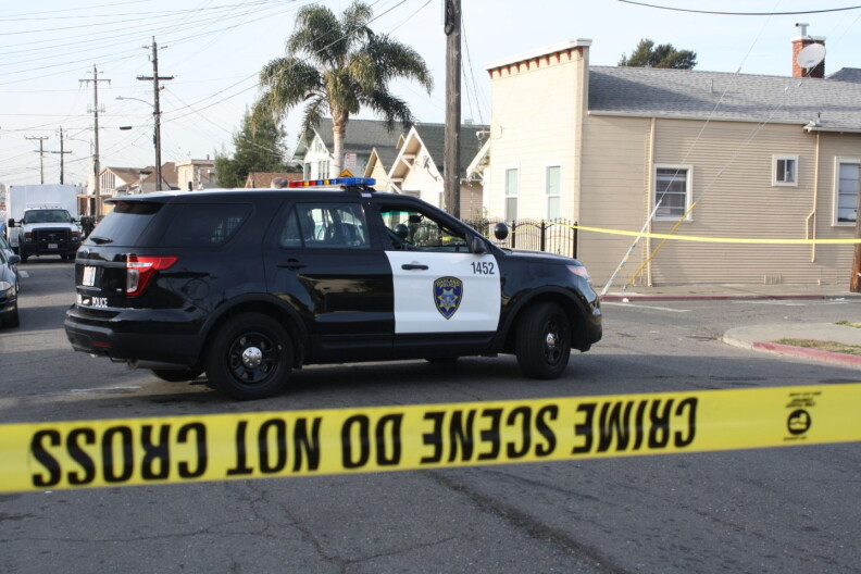A black and white SUV is parked in the middle of a street behind yellow, police crime tape.