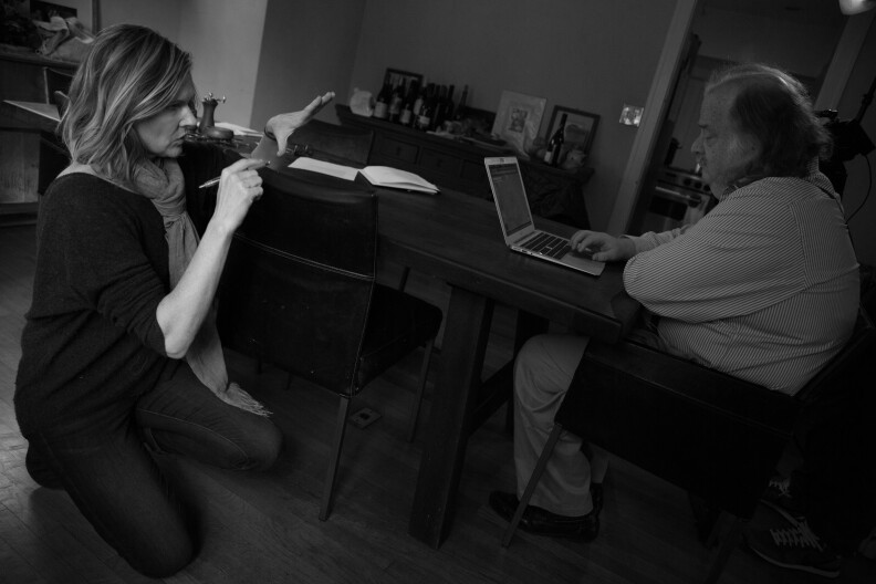 A female presenting person kneels in front of a male presenting person who sits at a desk in front of a computer.