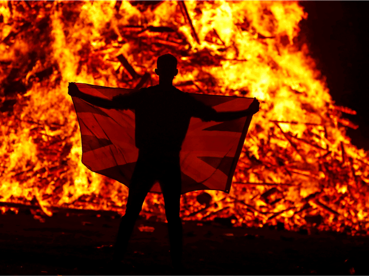 A male holds a flag in front of the Loyalist Corcrain Redmanville bonfire, which was lit to mark the start of the unionist 12 July celebrations, in Portadown, Northern Ireland, on 11 July 2021.