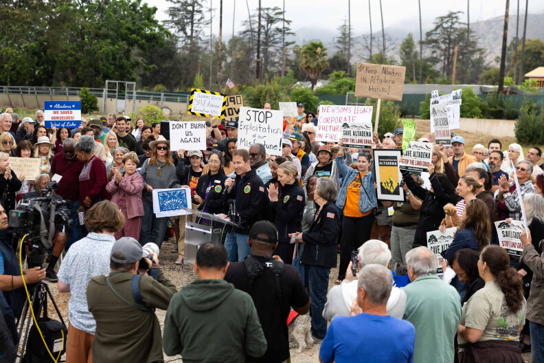 A man speaks at a news conference, surrounded by people holding signs.