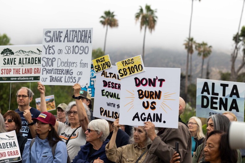 People hold signs saying "Don't burn us again" and "Pass SB 1090."