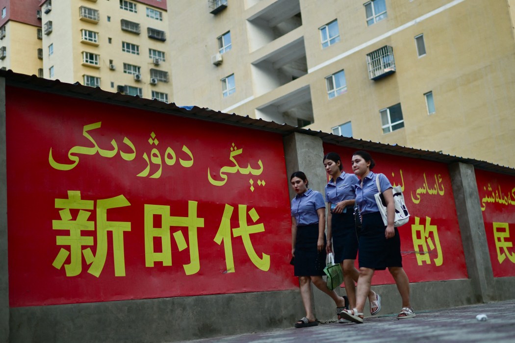 This picture taken on July 18, 2023, shows women walking past a propaganda slogan promoting ethnic unity in the new era, in both Chinese and Uyghur languages, in Yarkant, northwestern China's Xinjiang region. Photo: Pedro Pardo/AFP.