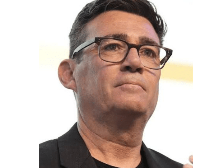 Head shot of Andy Burnham, wearing thick rimmed glasses, a crew neck tshirt and a blazer on top looking in the distance with quiet confidence. However, he has ruffled Scottish feathers.