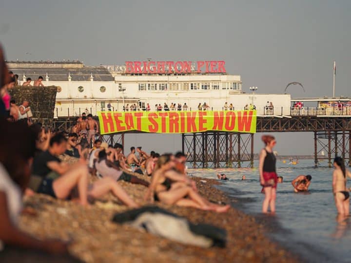 A banner hanging from Brighton pier reads Heat Strike Now as campaigners demand maximum working temperature