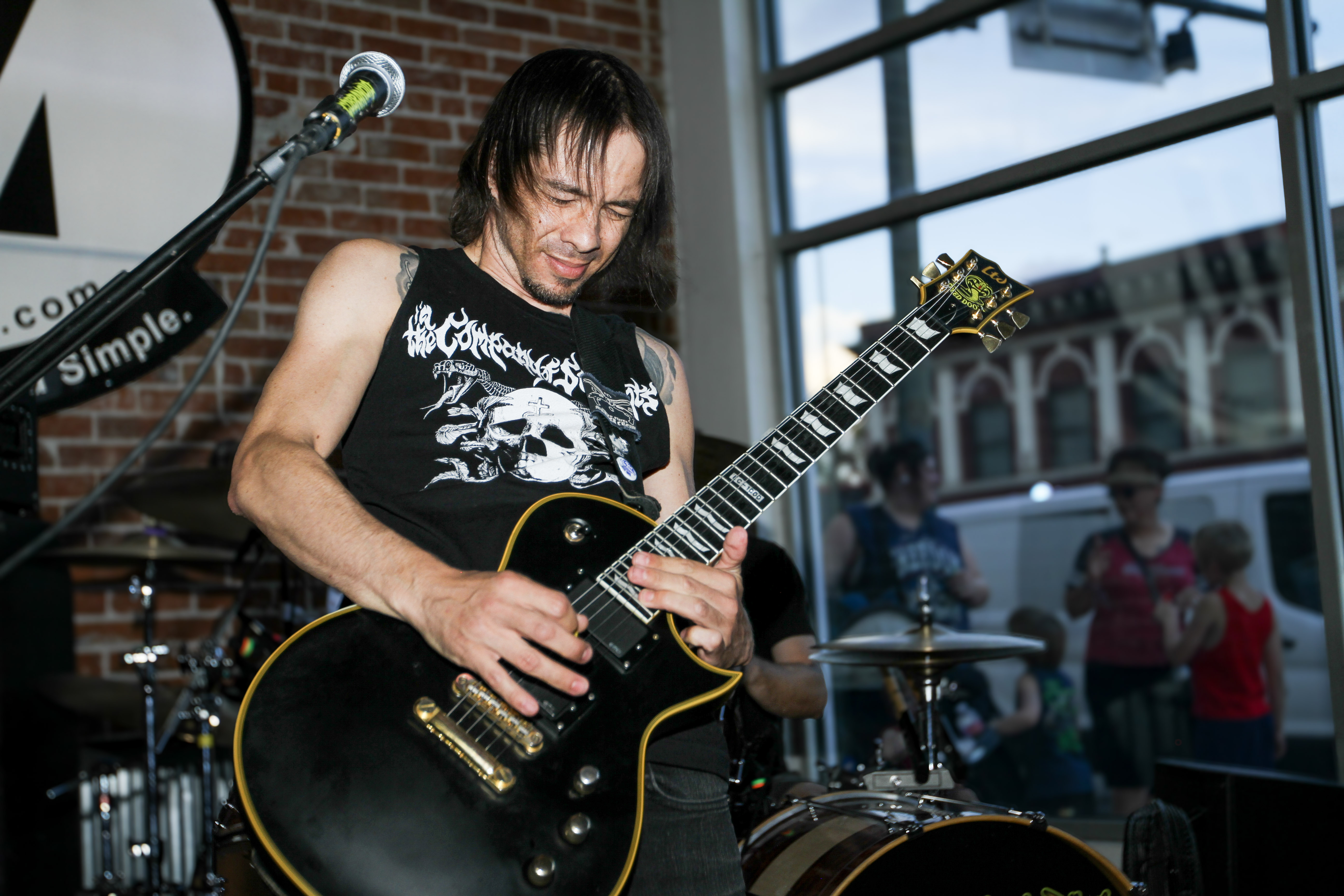 A guitarist in a metal band shreds inside an auto mechanic shop. A family with young kids watch through the window.