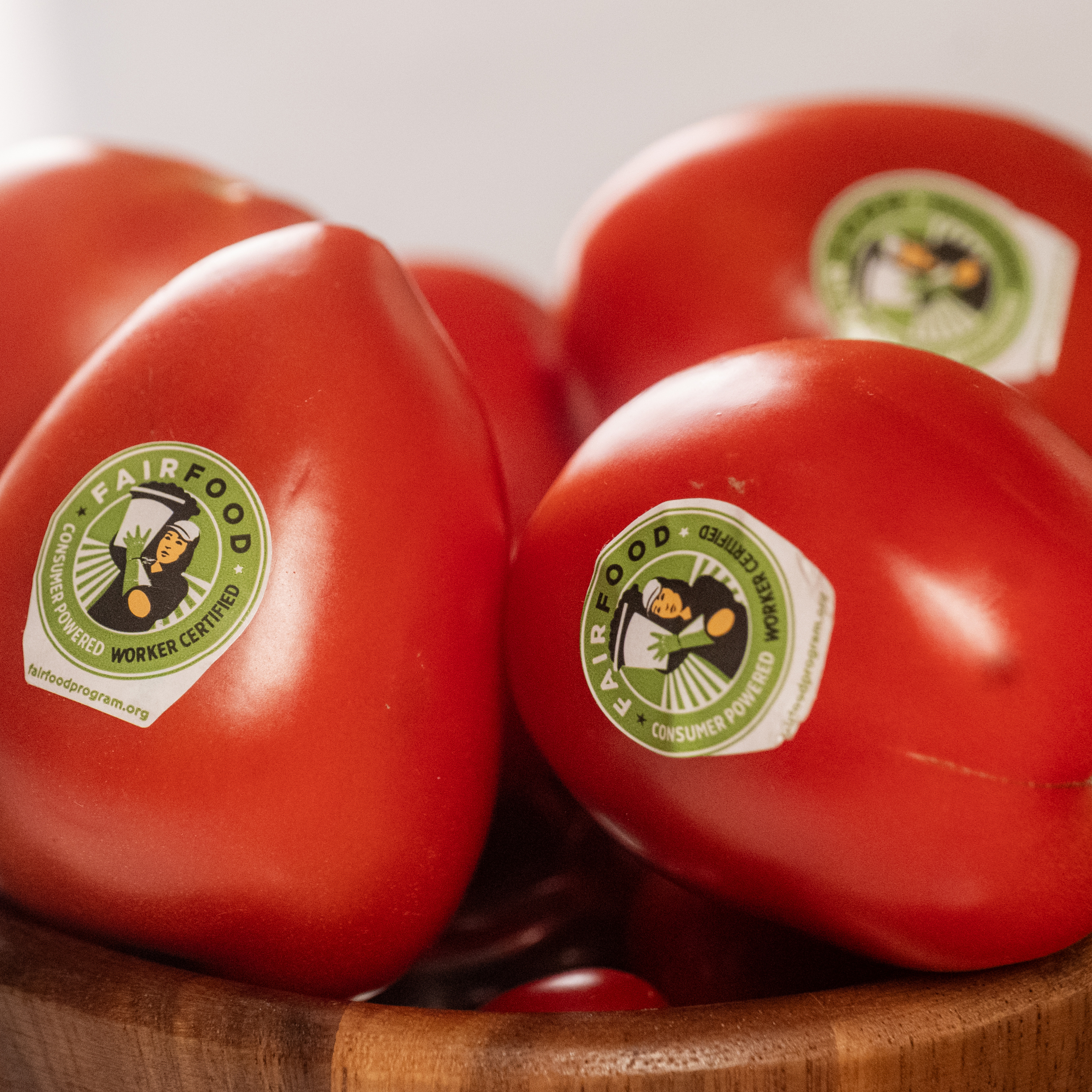 Tomatoes with βFair Foodβ stickers in a wooden bowl.