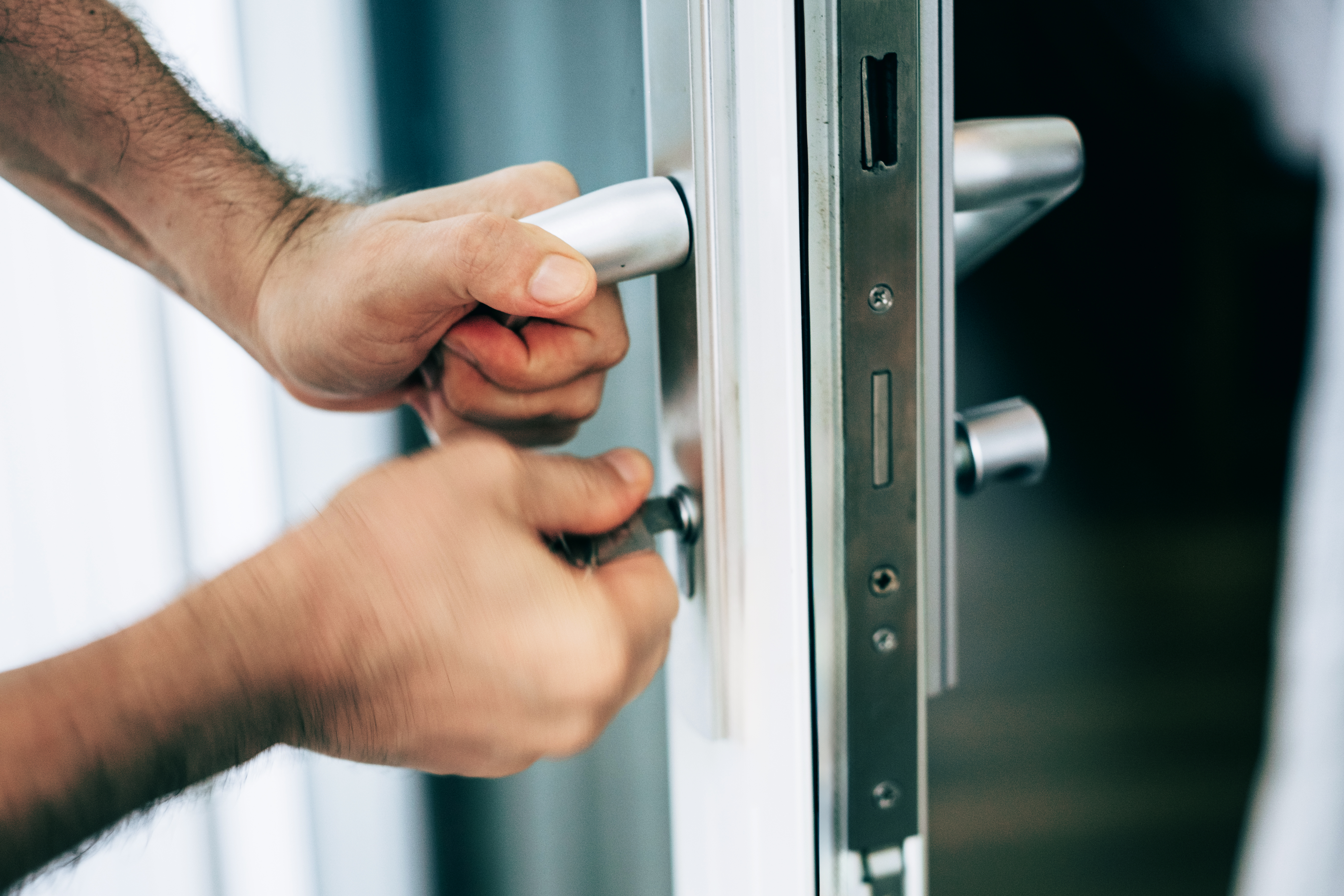 Close-up of hands unlocking a modern metallic door with a key