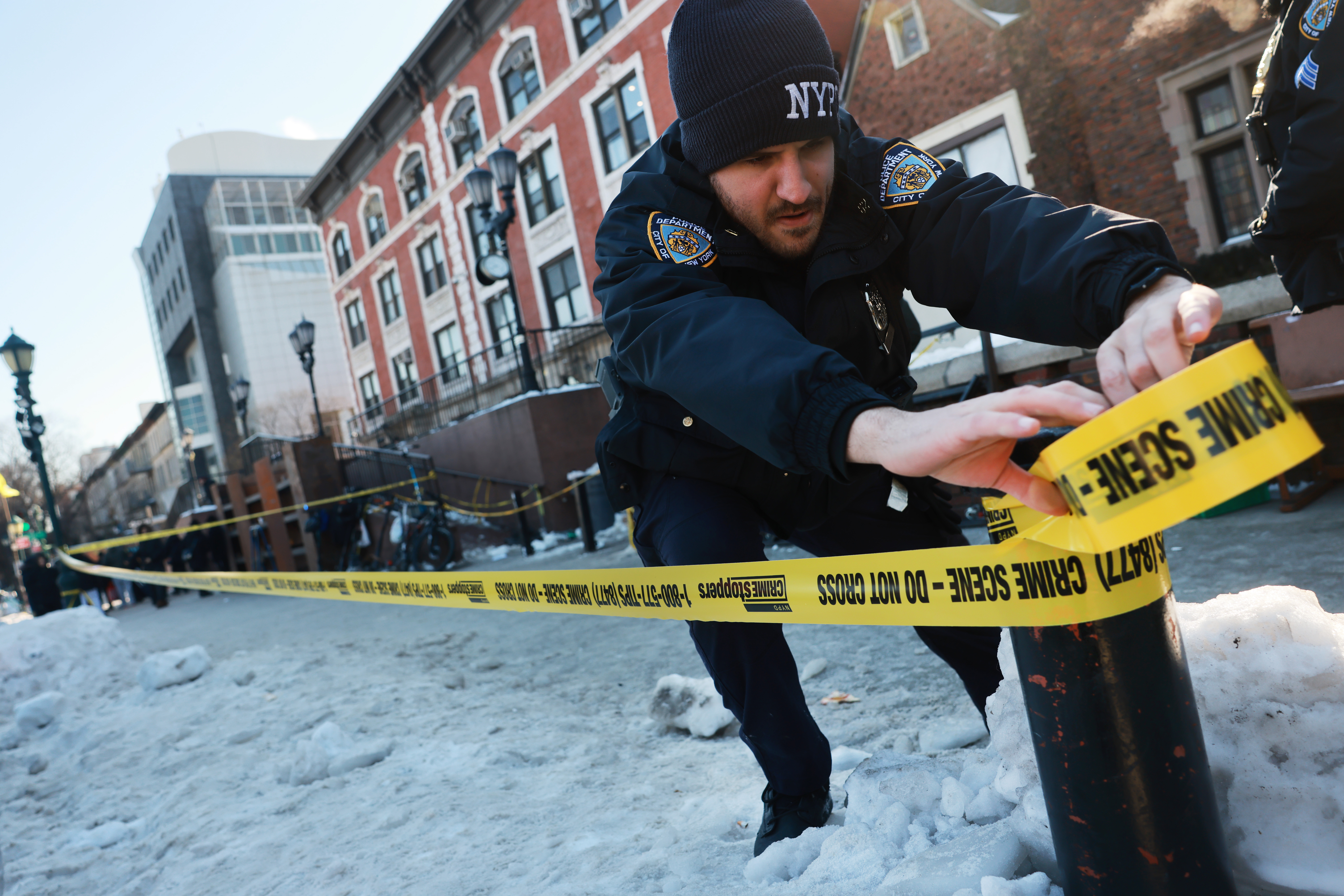 Police put up crime scene tape as members of the Hasidic Jewish community gather outside of the Chabad Lubavitch world headquarters.
