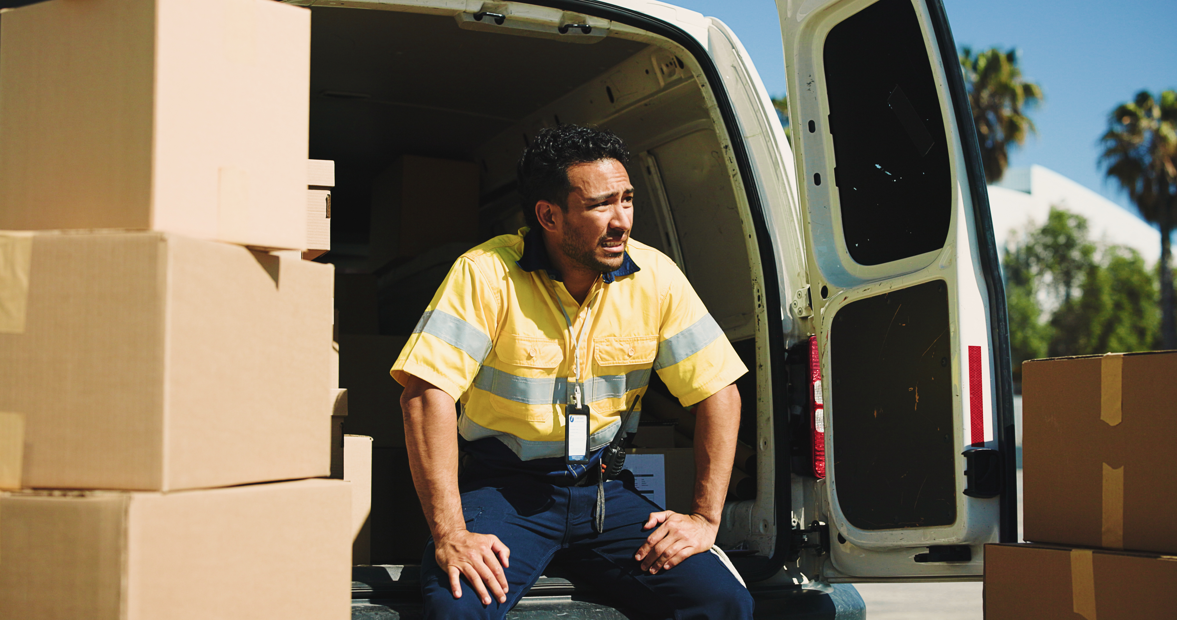 A delivery worker sits at the edge of a van on a hot day.