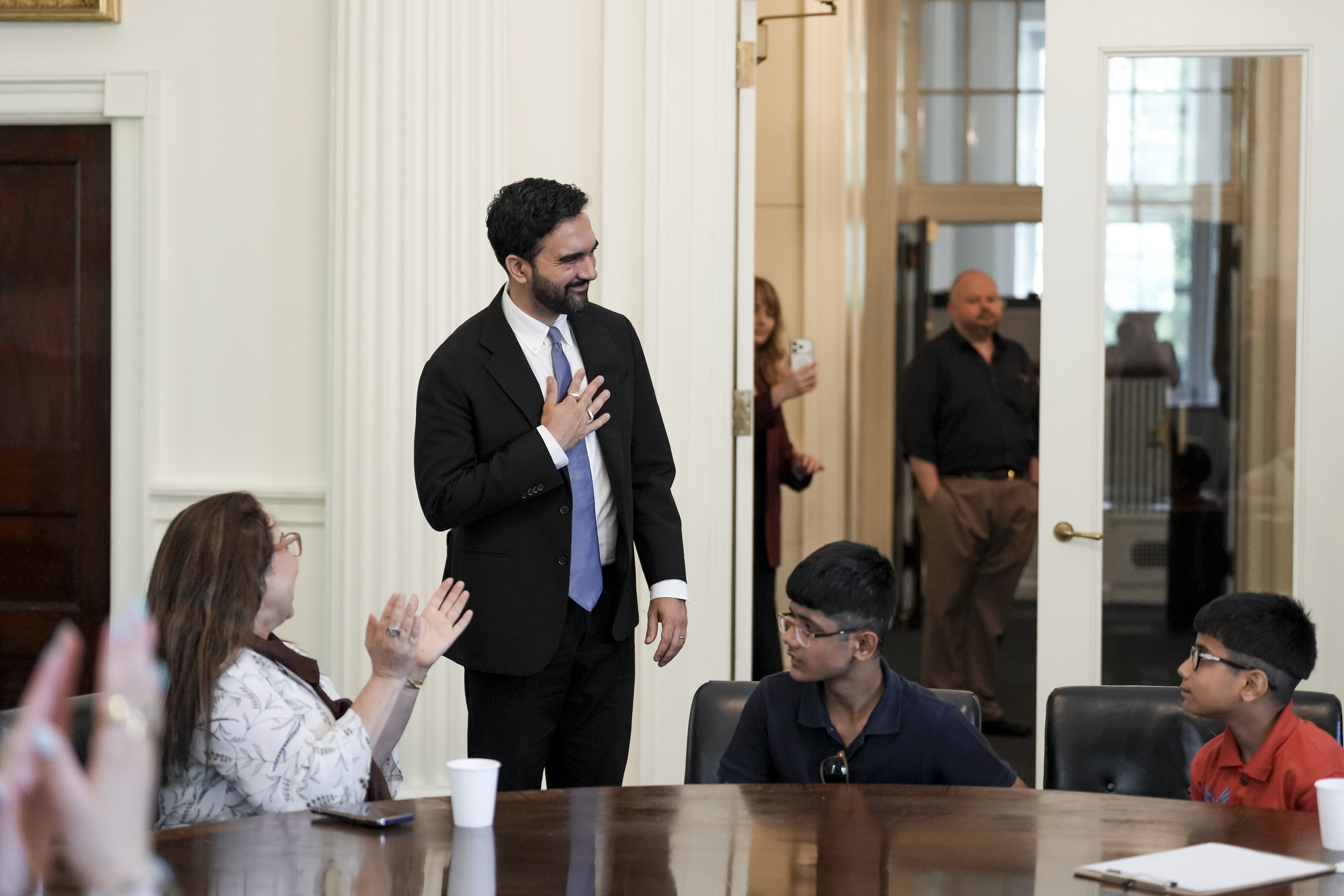 Mayor Mamdani greets people sitting at a table.