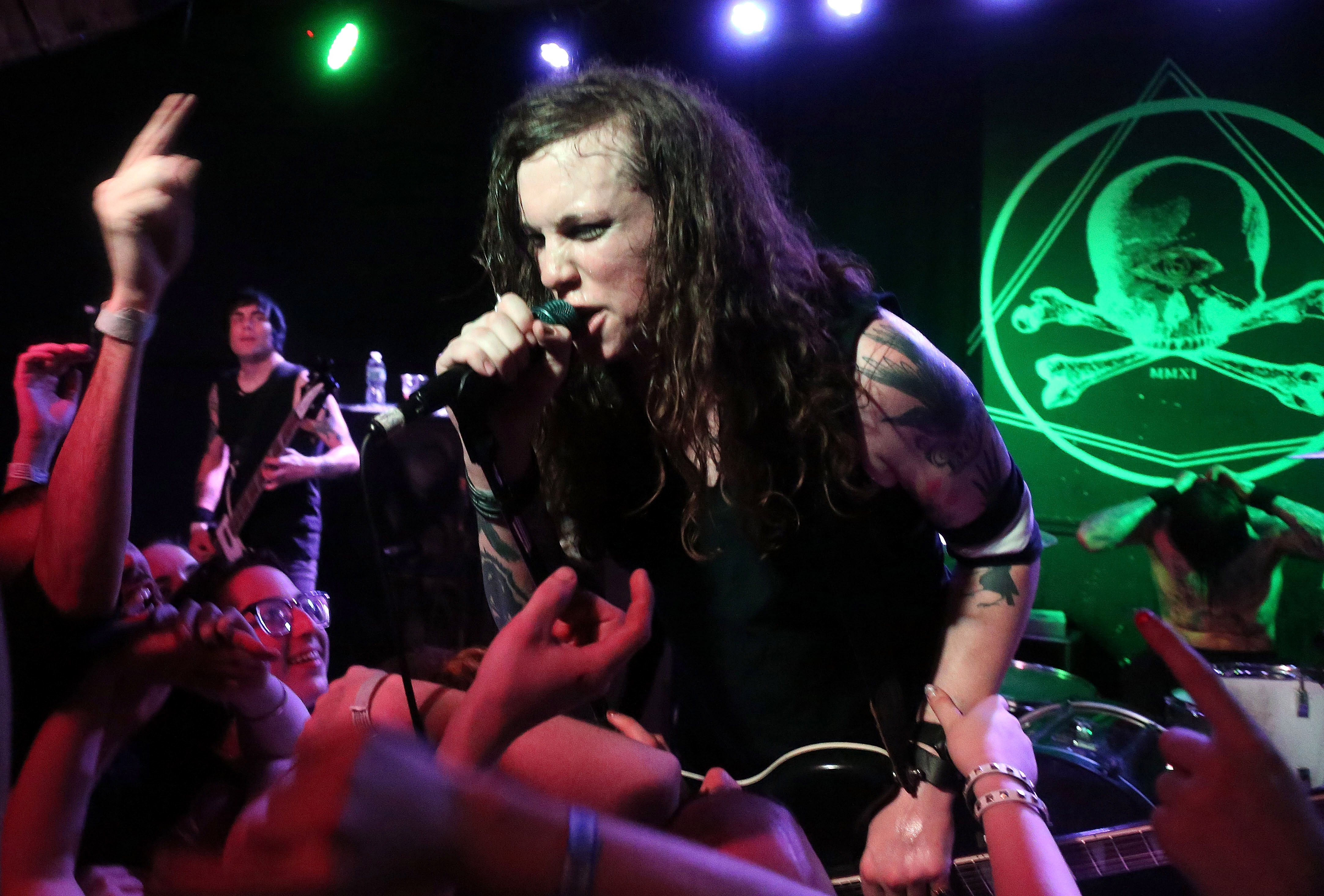 A tattooed person singing into a microphone with the crowd jumping up to sing alone