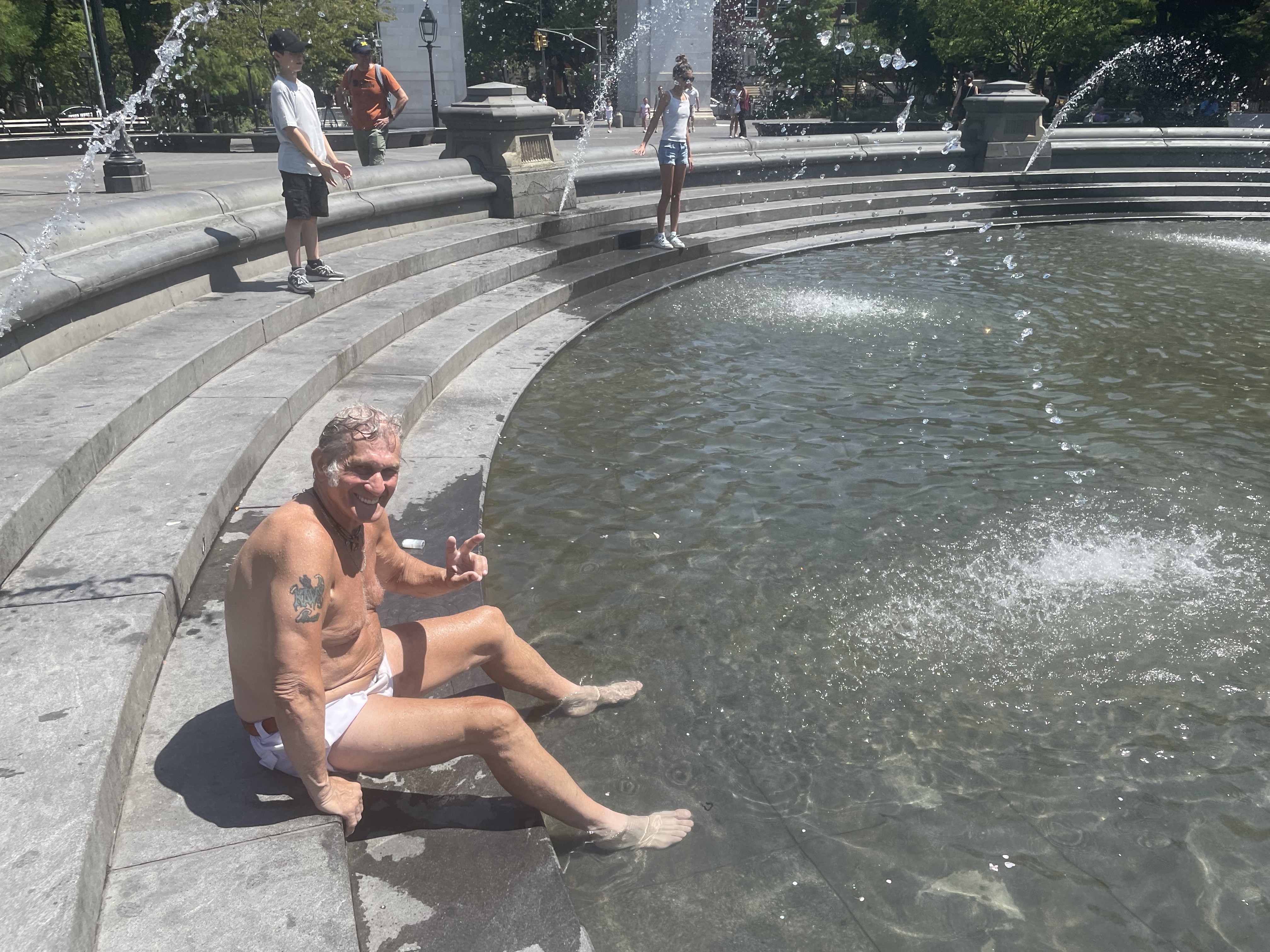 A man sits in a fountain and cools his feet.