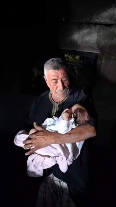 The grandfather of baby Lana Shahada, whose home was attacked by Israeli settlers, holds her and looks down at her