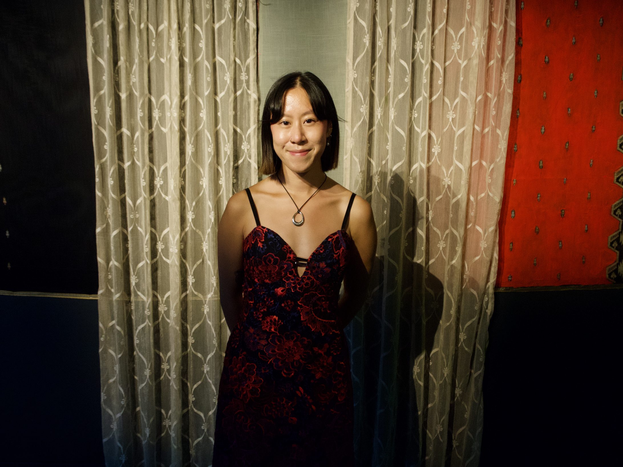 A woman stands before a lace and fabric background
