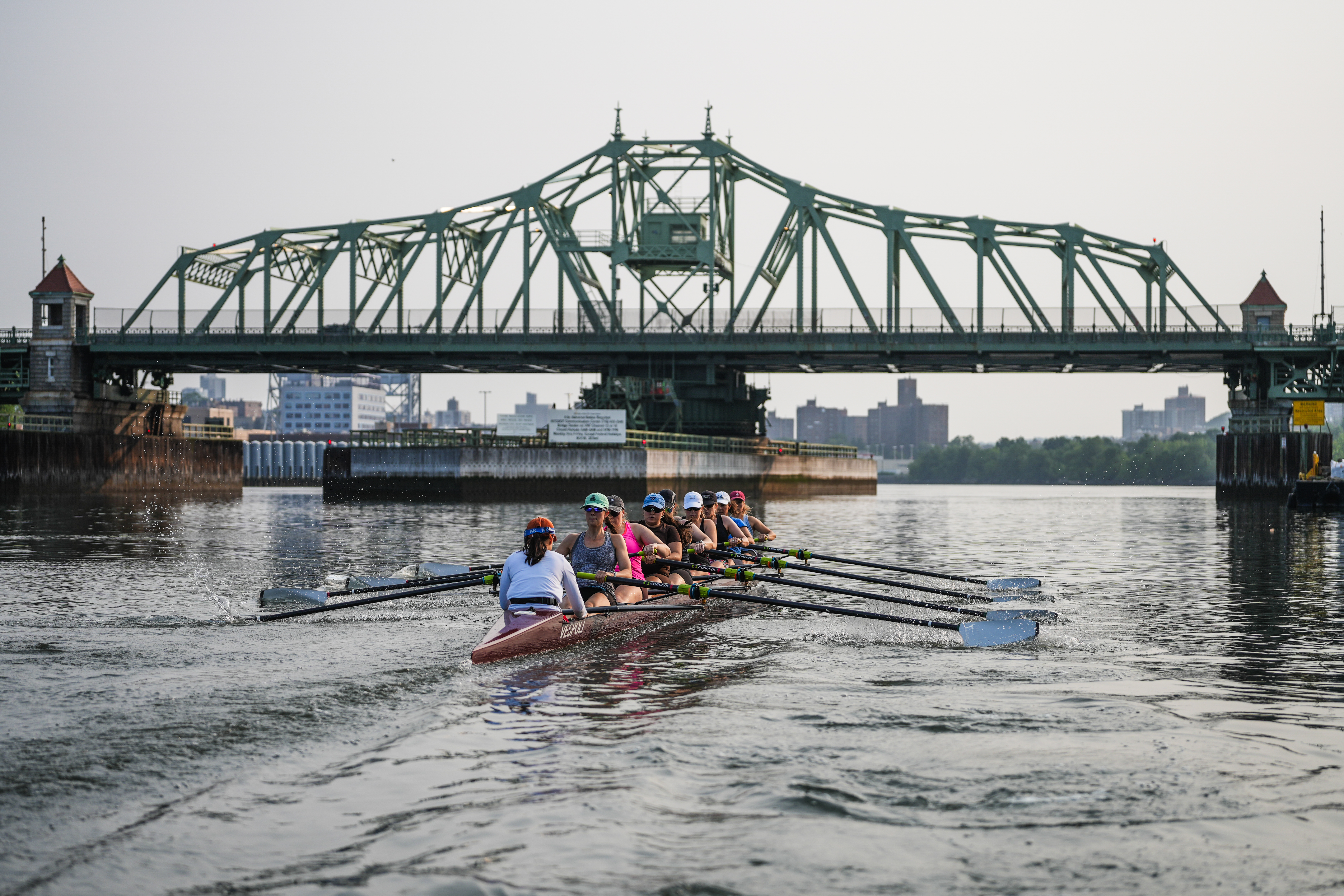 People row on a shell boat underneath a bridge.