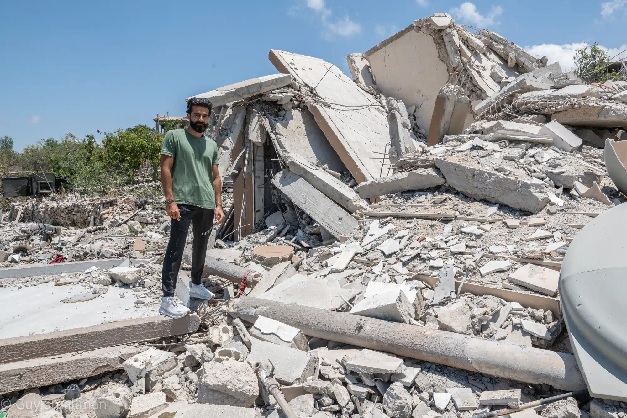 Ali, a young Lebanese man, standing in the rubble of a destroyed building in South Lebanon