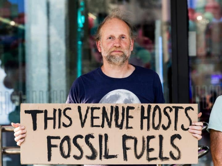 QEII fossil fuel protest Protester holds sign saying This Venue Hosts Fossil Fuels