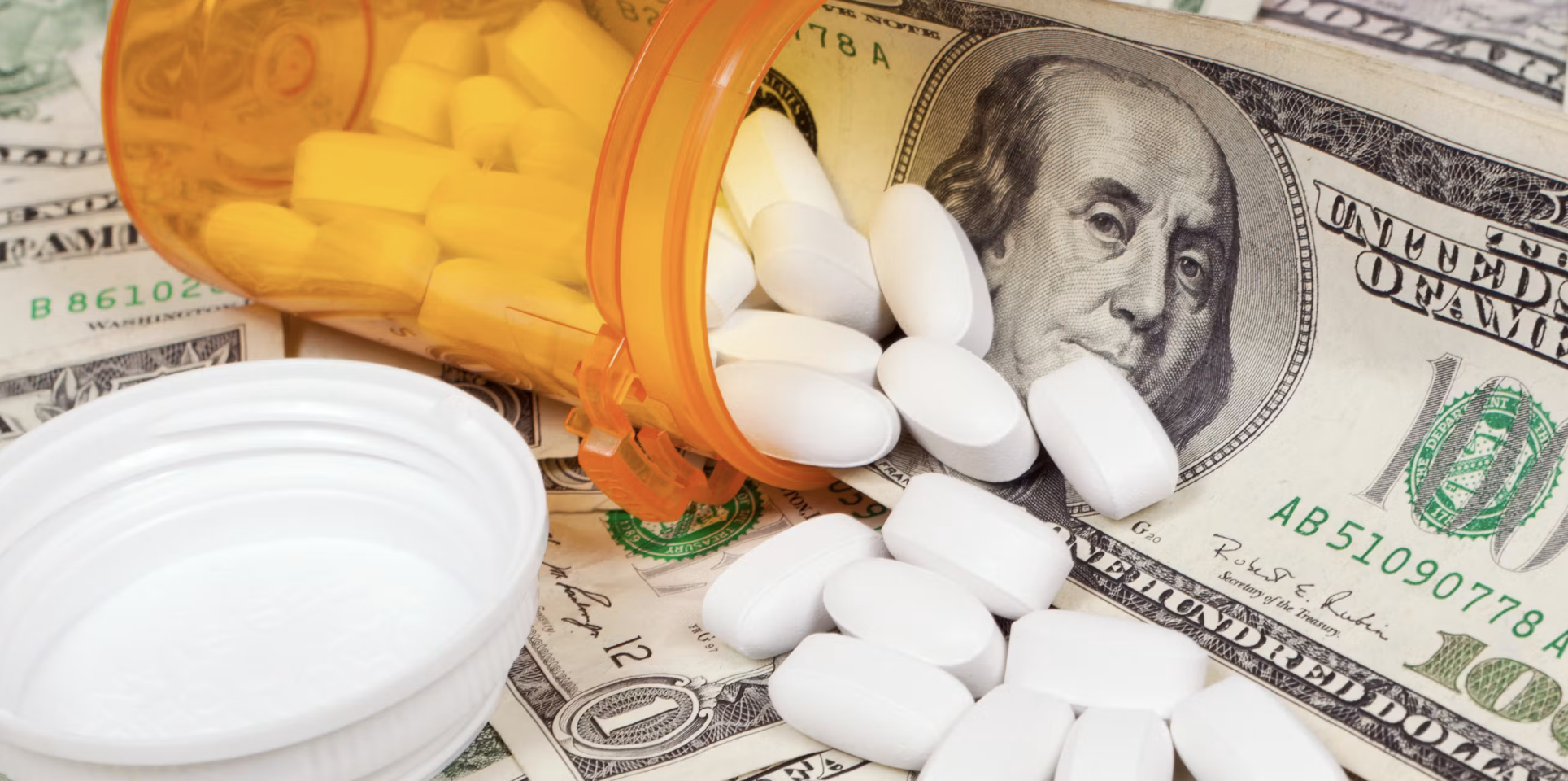 A prescription bottle and pills sit next to $100 bills
