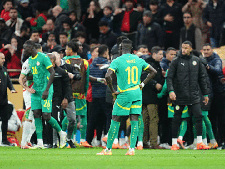 Senegal players standing on the pitch at AFCON final, some wearing only their kits and others with puffer jackets on