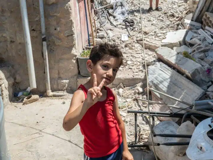 A young boy doing a victory sign in front of rubble in South Lebanon