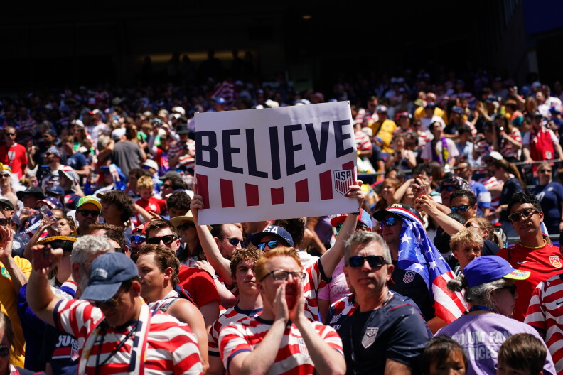 A fan holds a sign reading "Believe" in a crowd of fans in red, white and blue.