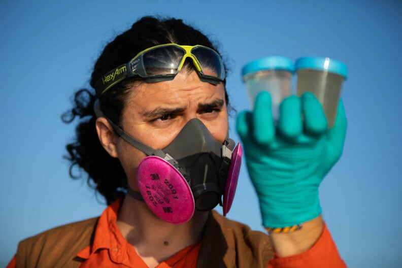A man with curly hair inspects water samples while wearing a respiratory mask.