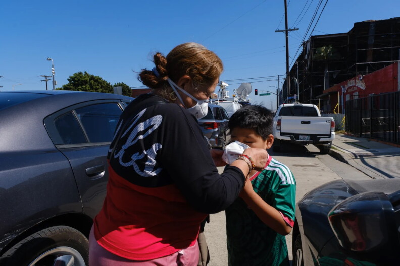 A woman wearing a respiratory mask outside affixes one to a boy.